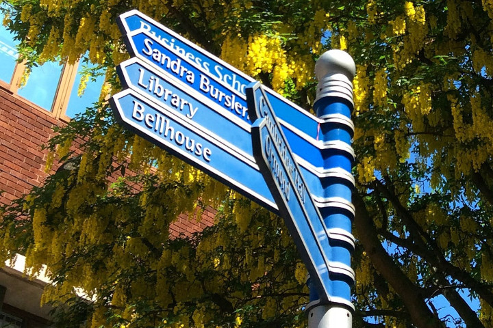 A blue signpost with directions to various places on the MMU campus